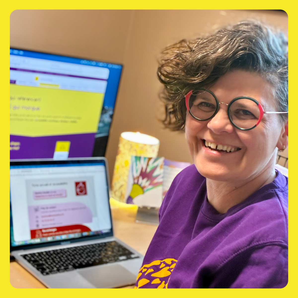 Béatrice Schaller-Le Leu à son bureau. Elle est souriante et porte des lunettes de vue. Elle est assise à son bureau. on voit son ordinateur portable derrière elle sur lequel est affiché une fiche d'accueil. Et sur un écran plus grand son site