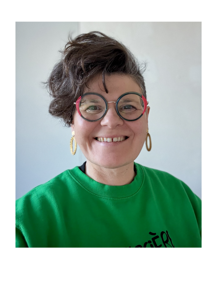 Beatrice Schaller-Le Leu, rédactrice inclusive. Elle apparait souriante. Elle porte des lunettes, a les cheveux rasés sur le côté gauche et une mèche sur le côté droit. Elle porte un sweat vert et des boucles d'oreilles en or végétal.